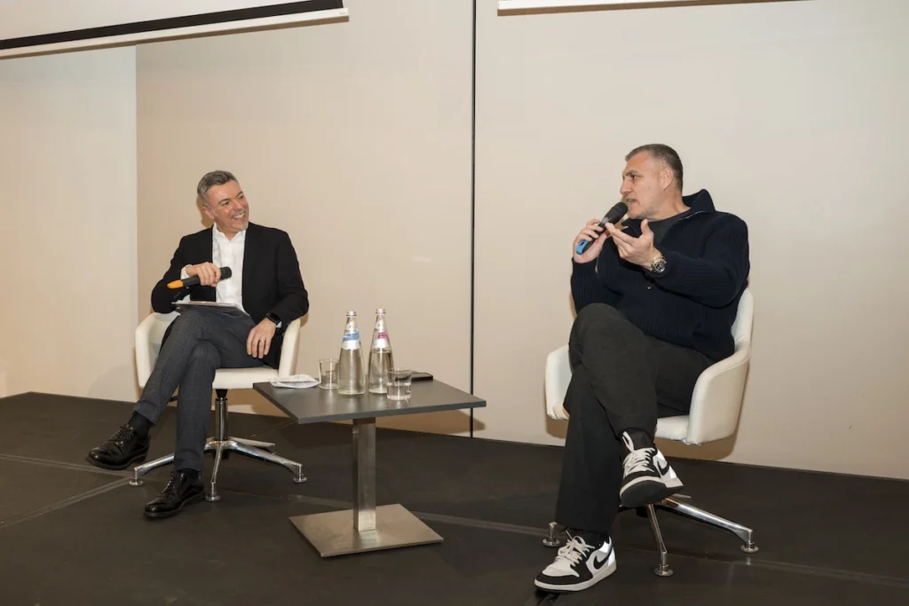 Il presentatore Attilio Reinhardt, seduto a sinistra, intervista Christian Vieri, seduto a destra, entrambi con microfoni in mano sul palco dell'Hotel Sheraton San Siro di Milano.